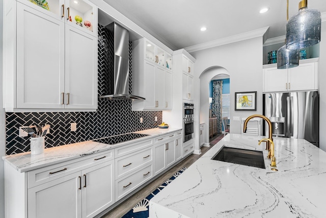 kitchen with white cabinetry, sink, wall chimney range hood, stainless steel fridge, and decorative light fixtures