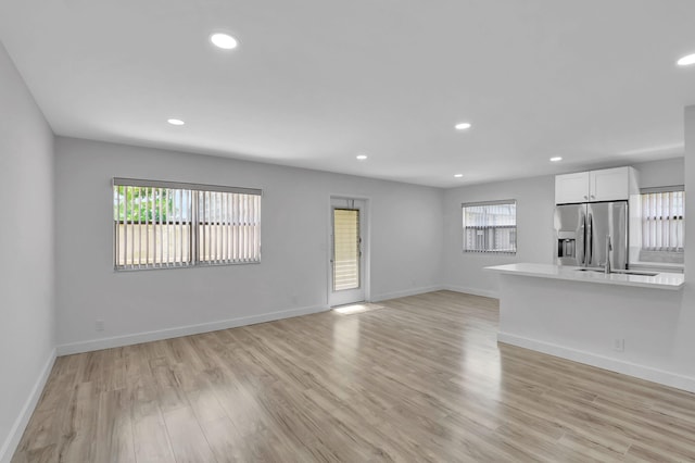 unfurnished living room with recessed lighting, baseboards, a sink, and light wood finished floors