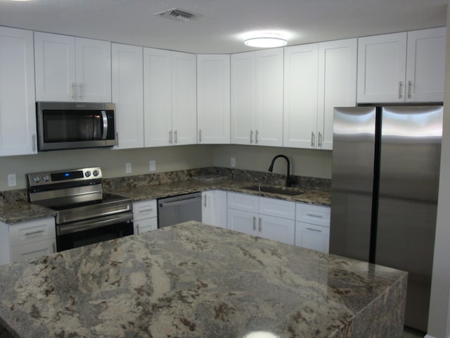 kitchen with dark stone countertops, white cabinetry, sink, and stainless steel appliances