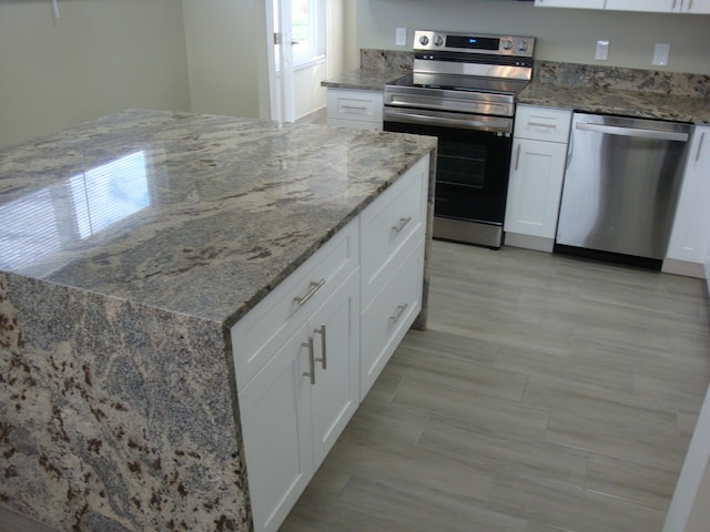 kitchen featuring light stone countertops, white cabinets, stainless steel appliances, and light tile patterned floors