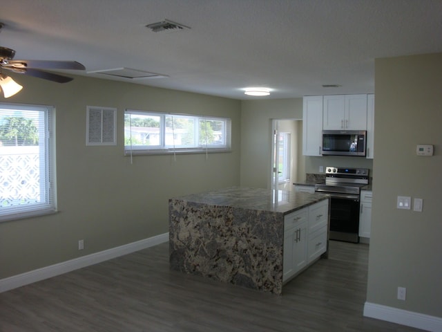 kitchen featuring white cabinets, a kitchen island, stainless steel appliances, and dark stone counters