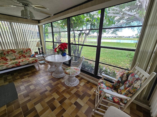 sunroom with ceiling fan and a water view