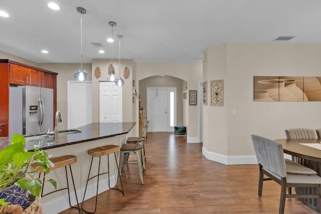 kitchen with stainless steel fridge, dark hardwood / wood-style flooring, sink, pendant lighting, and dark stone countertops