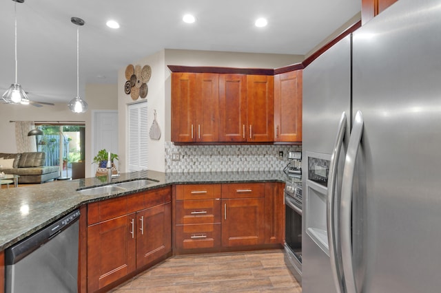 kitchen with backsplash, stainless steel appliances, sink, dark stone countertops, and hanging light fixtures