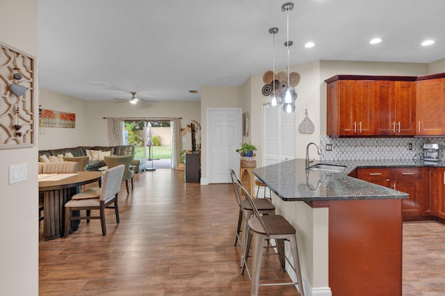 kitchen featuring ceiling fan, sink, kitchen peninsula, dark stone countertops, and pendant lighting