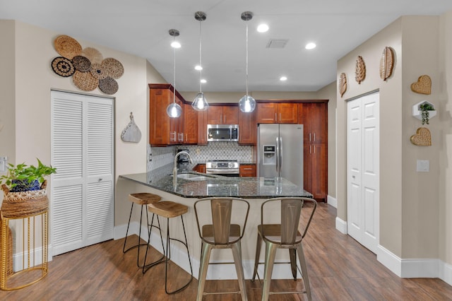 kitchen with kitchen peninsula, appliances with stainless steel finishes, backsplash, dark wood-type flooring, and pendant lighting