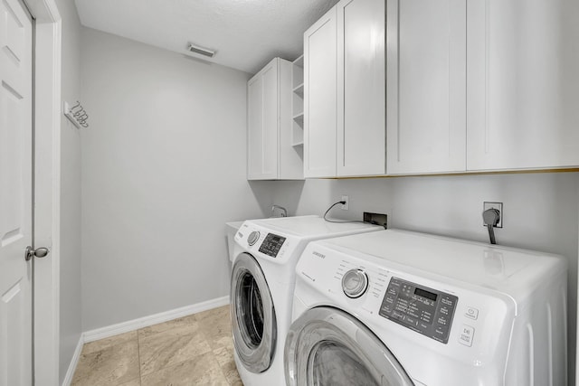 laundry room featuring washer and clothes dryer, cabinets, and a textured ceiling