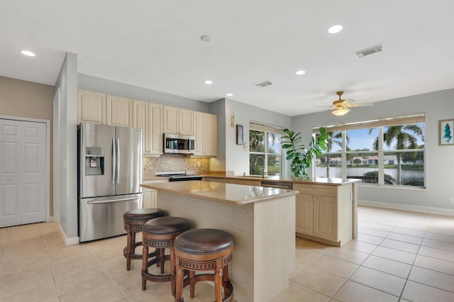 kitchen featuring tasteful backsplash, visible vents, appliances with stainless steel finishes, a center island, and cream cabinetry