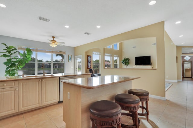 kitchen featuring light brown cabinets, a sink, visible vents, stainless steel dishwasher, and a center island