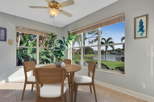 dining room featuring light tile patterned floors, ceiling fan, a water view, and baseboards