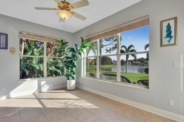 tiled spare room with a water view, ceiling fan, and baseboards