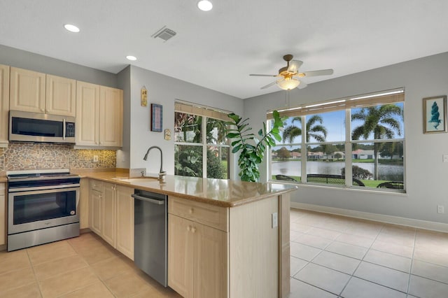 kitchen with a peninsula, stainless steel appliances, light brown cabinetry, a sink, and light tile patterned flooring