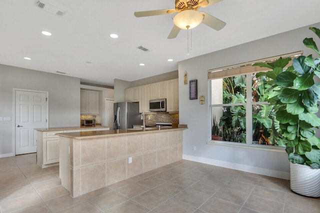 kitchen featuring light tile patterned flooring, stainless steel appliances, a peninsula, visible vents, and backsplash