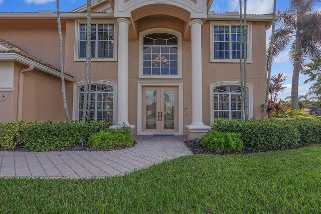 view of exterior entry featuring french doors, a lawn, and stucco siding