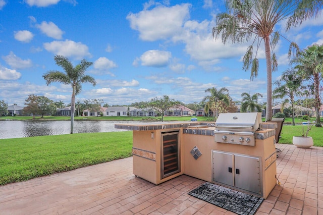 view of patio / terrace featuring beverage cooler, an outdoor kitchen, grilling area, and a water view