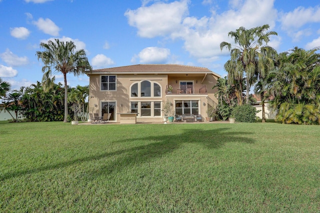 back of house featuring a balcony, a patio area, a lawn, and stucco siding