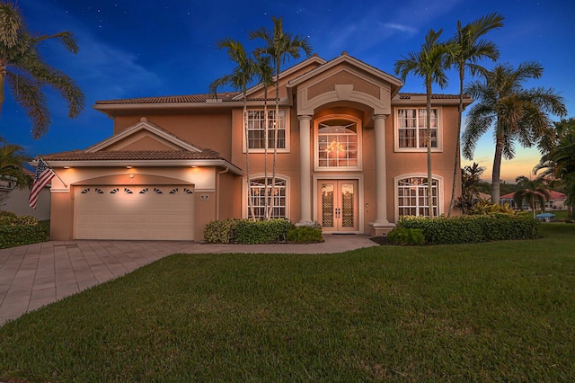 mediterranean / spanish-style house with an attached garage, driveway, french doors, stucco siding, and a front lawn