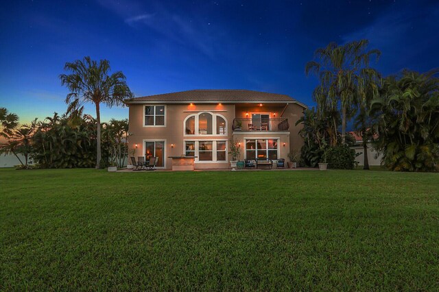 back of property with stucco siding, a patio, a balcony, and a lawn