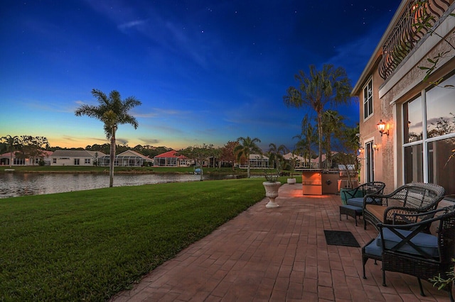 patio terrace at dusk with a residential view, a water view, and a lawn