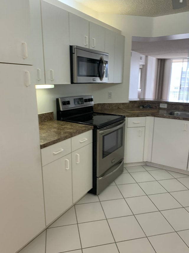 kitchen featuring white cabinetry, sink, light tile patterned floors, stainless steel appliances, and a textured ceiling