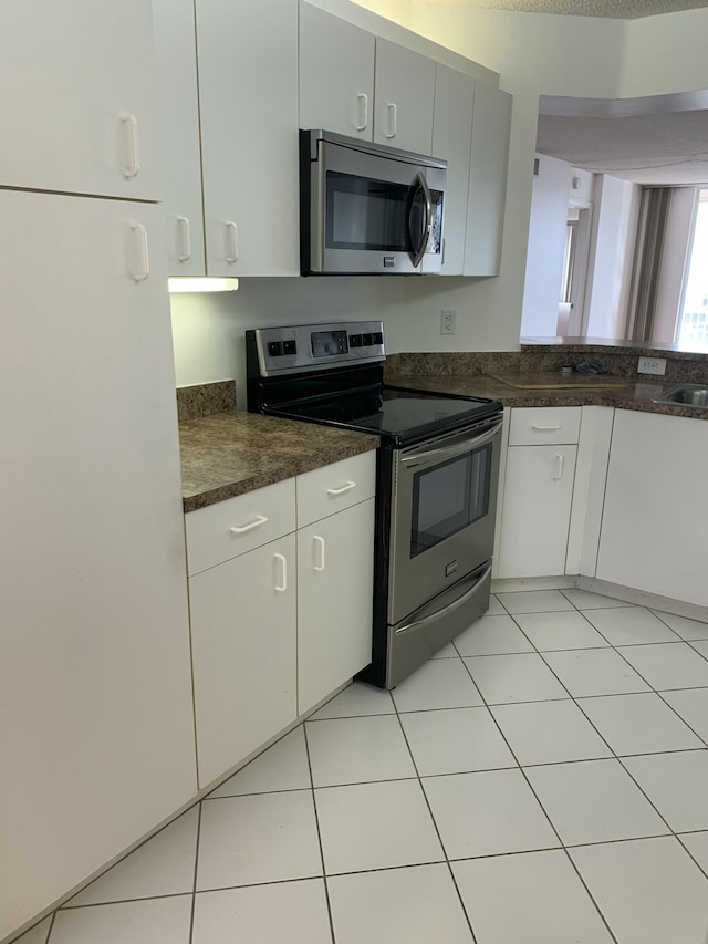 kitchen featuring appliances with stainless steel finishes, light tile patterned floors, and white cabinets