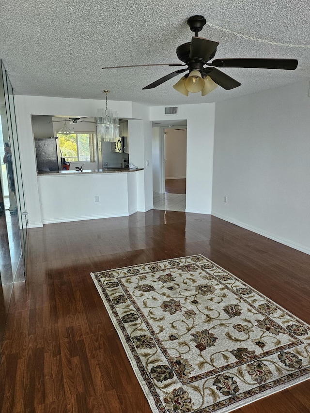 unfurnished living room featuring ceiling fan, dark hardwood / wood-style flooring, and a textured ceiling