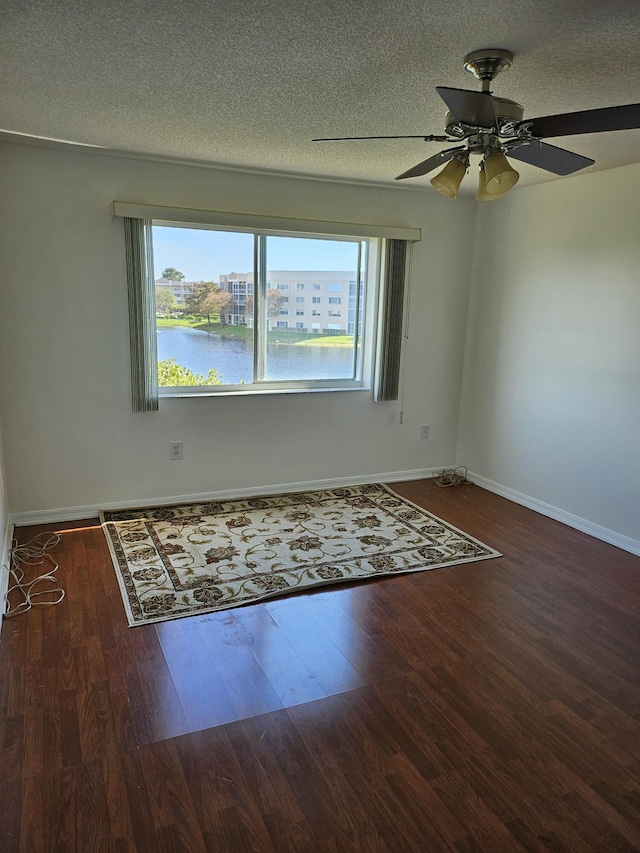 spare room featuring ceiling fan, dark hardwood / wood-style floors, a textured ceiling, and a water view