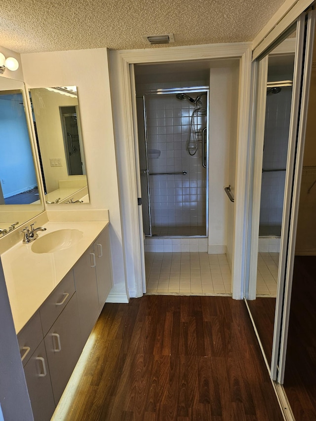 bathroom with vanity, hardwood / wood-style flooring, a textured ceiling, and tiled shower