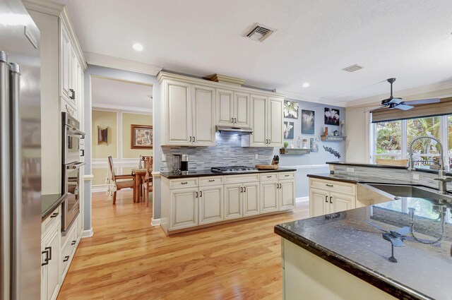 kitchen with appliances with stainless steel finishes, light wood-type flooring, ceiling fan, crown molding, and sink