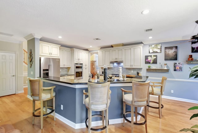 kitchen featuring a breakfast bar, appliances with stainless steel finishes, backsplash, and light wood-type flooring