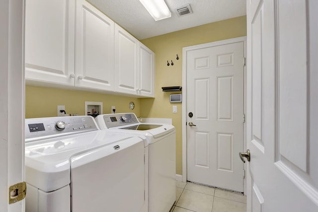 washroom featuring washer and dryer, light tile patterned floors, a textured ceiling, and cabinets