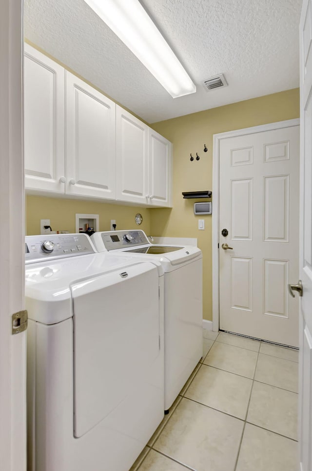 washroom with washer and clothes dryer, cabinets, light tile patterned floors, and a textured ceiling