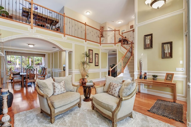 living room featuring wood-type flooring, ornate columns, crown molding, and a towering ceiling