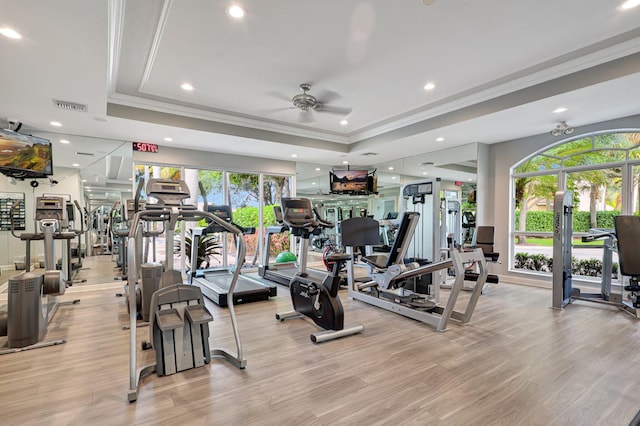 exercise room with ceiling fan, light hardwood / wood-style floors, a raised ceiling, and ornamental molding