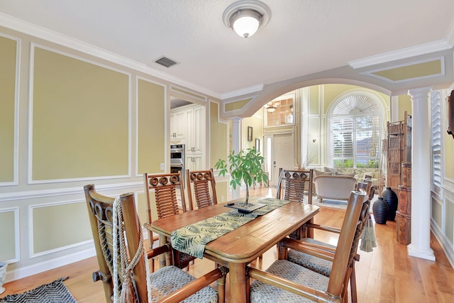 dining room with light hardwood / wood-style floors, crown molding, and decorative columns