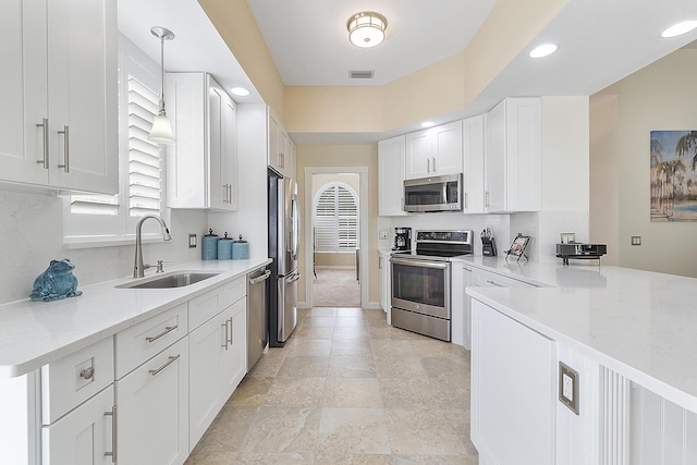 kitchen with light stone countertops, stainless steel appliances, sink, white cabinetry, and hanging light fixtures