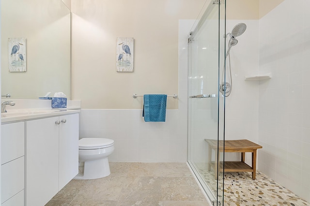 bathroom with vanity, toilet, a shower with shower door, and tile walls