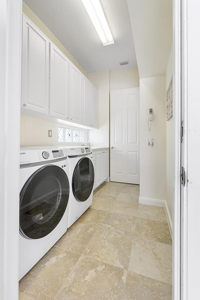 laundry room with cabinets, washing machine and dryer, and a textured ceiling