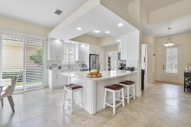 kitchen with appliances with stainless steel finishes, a breakfast bar, decorative light fixtures, white cabinets, and kitchen peninsula