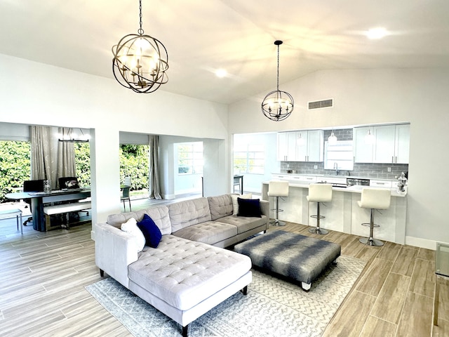 living room featuring a healthy amount of sunlight, vaulted ceiling, a notable chandelier, and sink