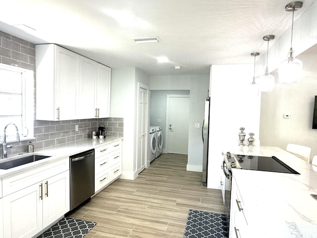 kitchen featuring stainless steel appliances, sink, decorative light fixtures, washing machine and dryer, and white cabinetry