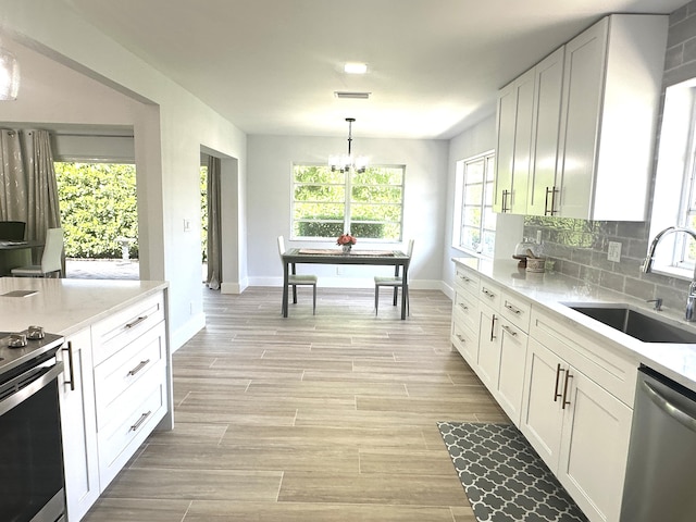 kitchen with sink, stainless steel appliances, tasteful backsplash, decorative light fixtures, and white cabinets