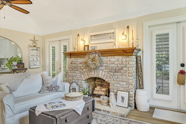 living room with ceiling fan, vaulted ceiling, brick ceiling, a fireplace, and hardwood / wood-style flooring