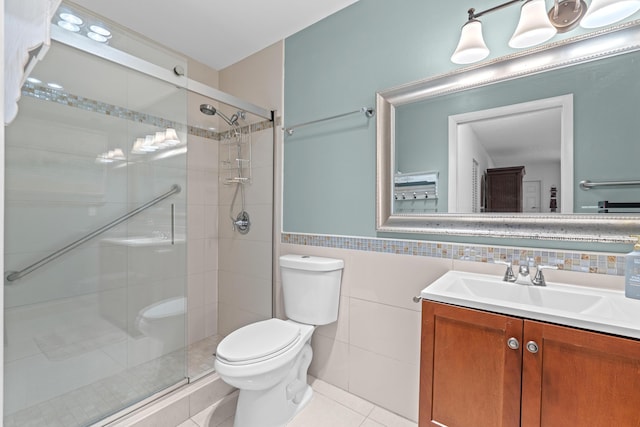 bathroom featuring tile patterned flooring, toilet, a shower with door, vanity, and tile walls