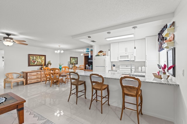 kitchen with white appliances, white cabinets, hanging light fixtures, light stone counters, and kitchen peninsula