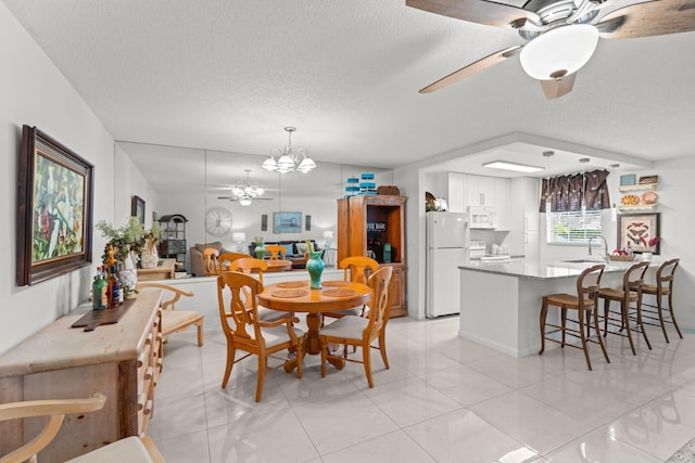 tiled dining area featuring sink, ceiling fan with notable chandelier, and a textured ceiling