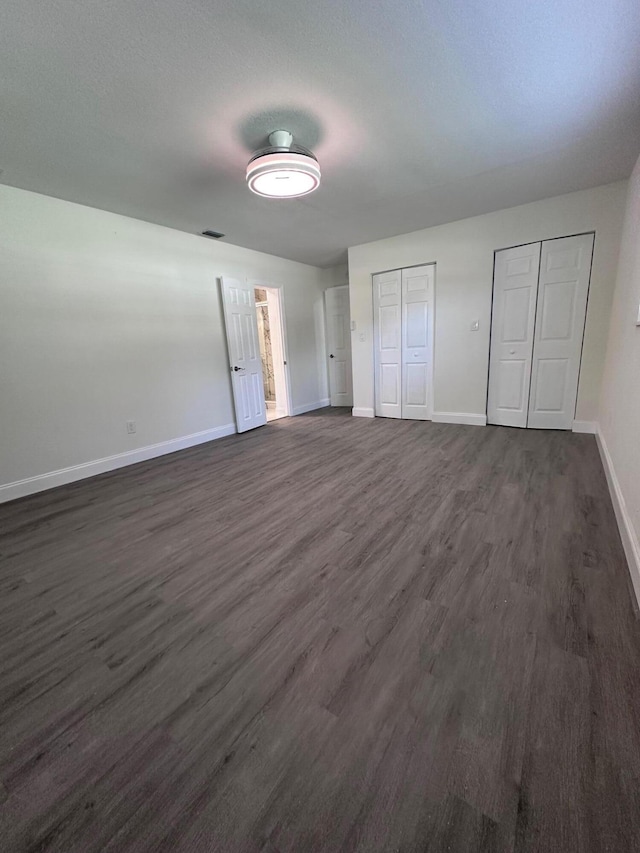 unfurnished bedroom with dark hardwood / wood-style flooring and two closets