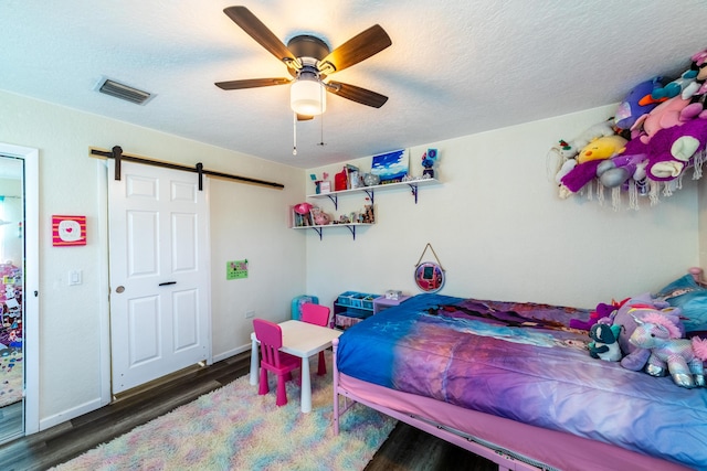 bedroom featuring dark hardwood / wood-style flooring, a barn door, a textured ceiling, and ceiling fan