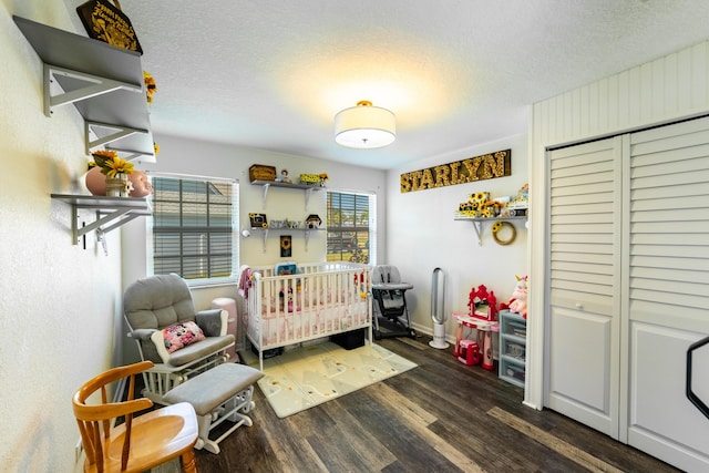 bedroom with dark hardwood / wood-style flooring, a crib, and a textured ceiling