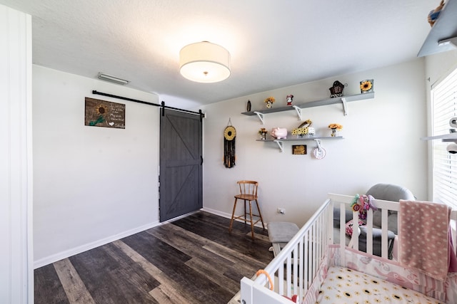 bedroom with a crib, dark hardwood / wood-style flooring, and a barn door